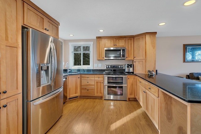 kitchen with light wood finished floors, recessed lighting, a peninsula, stainless steel appliances, and a sink