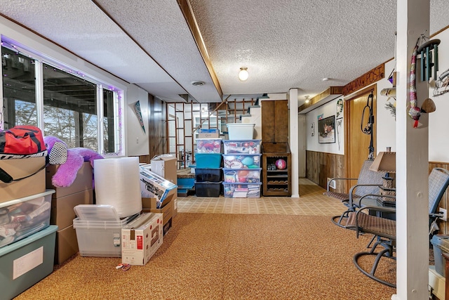 below grade area featuring wooden walls, a wainscoted wall, stairs, carpet flooring, and a textured ceiling