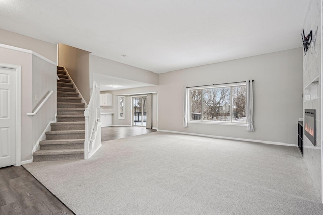 unfurnished living room featuring dark colored carpet, stairway, a fireplace, and baseboards