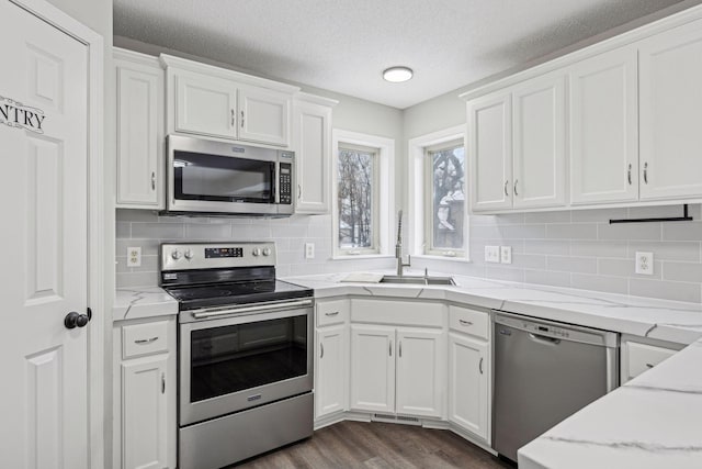 kitchen featuring dark wood finished floors, white cabinets, light stone counters, appliances with stainless steel finishes, and a sink