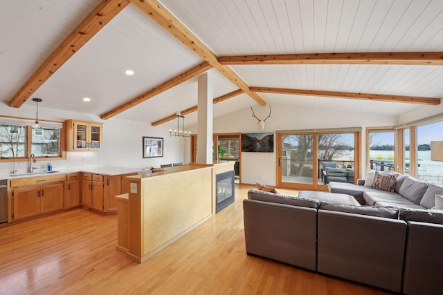 living room with light wood finished floors, recessed lighting, lofted ceiling with beams, an inviting chandelier, and a glass covered fireplace