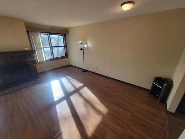 unfurnished living room with a fireplace, dark hardwood / wood-style flooring, heating unit, and a textured ceiling