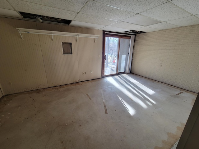 basement featuring a paneled ceiling and brick wall