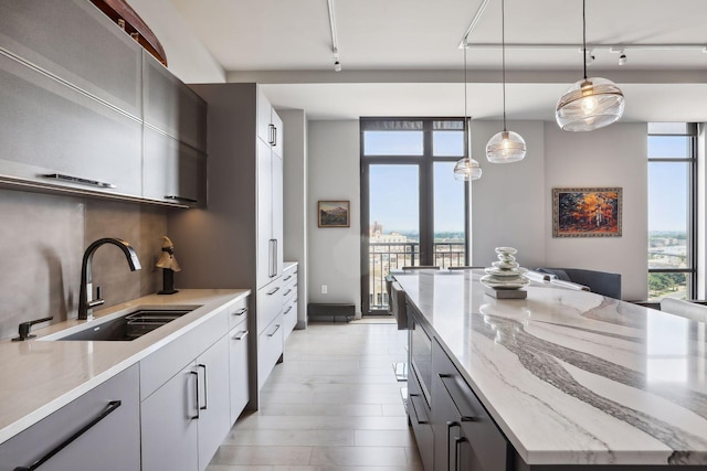 kitchen with floor to ceiling windows, rail lighting, sink, light stone counters, and decorative light fixtures