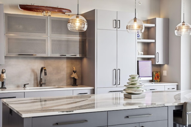 bar featuring gray cabinets, light stone countertops, hanging light fixtures, and sink