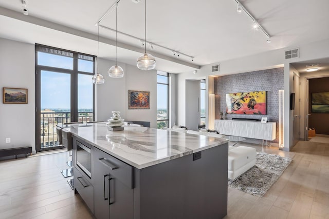 kitchen with a kitchen island, pendant lighting, stainless steel microwave, light stone counters, and light hardwood / wood-style floors