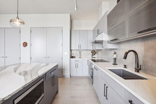 201 11th St Unit 1140, Minneapolis, MN 55403 - kitchen featuring decorative backsplash, under cabinet range hood, a sink, hanging light fixtures, and stainless steel appliances