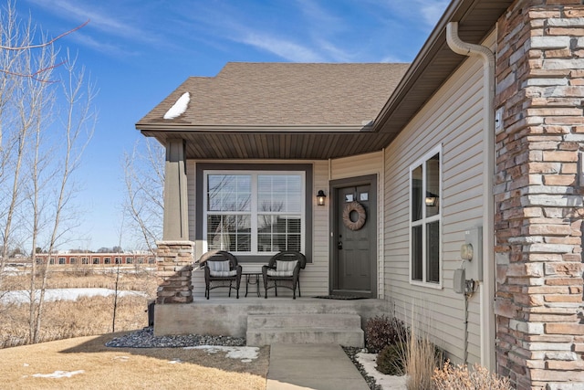 property entrance with a porch, stone siding, and roof with shingles