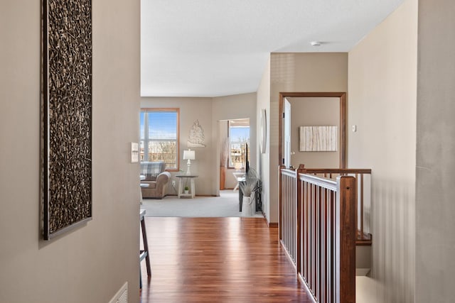 hallway with an upstairs landing, wood finished floors, visible vents, and a textured ceiling