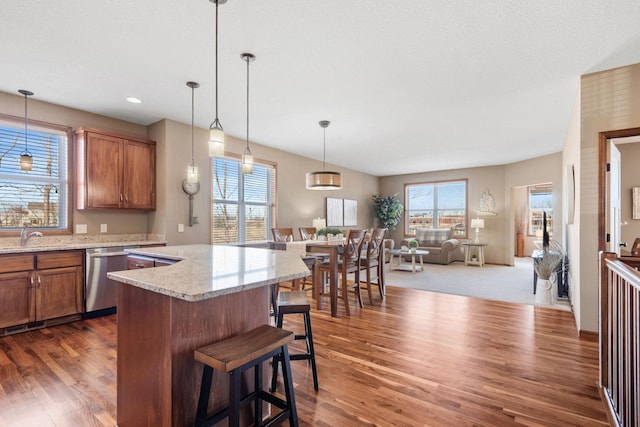 kitchen featuring dark wood-style floors, brown cabinetry, stainless steel dishwasher, open floor plan, and a center island