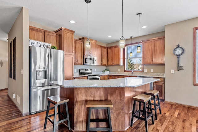 kitchen featuring decorative light fixtures, a kitchen breakfast bar, stainless steel appliances, and light wood-style floors