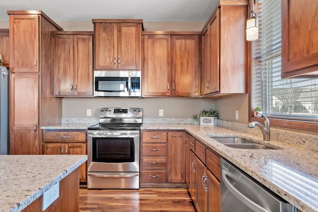 kitchen featuring brown cabinets, a sink, stainless steel appliances, light wood-style floors, and light stone countertops