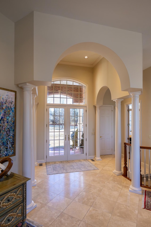 tiled foyer featuring crown molding, a towering ceiling, decorative columns, and french doors