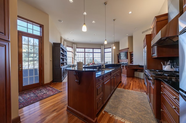 kitchen featuring extractor fan, a breakfast bar, sink, hanging light fixtures, and a kitchen island with sink