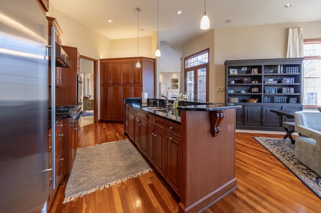 kitchen with stainless steel refrigerator, dark wood-type flooring, a kitchen island with sink, and pendant lighting