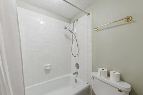 bathroom with toilet, tiled shower / bath combo, and a textured ceiling