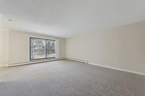 carpeted empty room featuring a baseboard heating unit and a textured ceiling