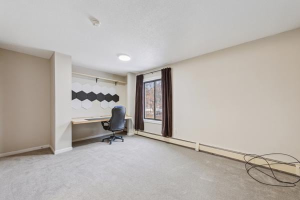 home office with built in desk, a baseboard heating unit, and light colored carpet