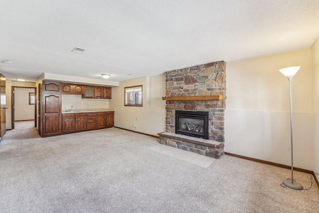 unfurnished living room featuring a fireplace, sink, light carpet, and a textured ceiling