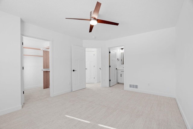 unfurnished bedroom with ensuite bathroom, a walk in closet, light carpet, and ceiling fan