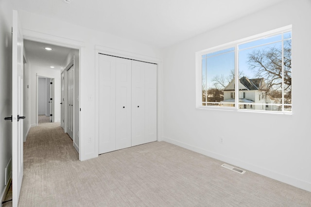 unfurnished bedroom featuring multiple windows, light carpet, and a closet