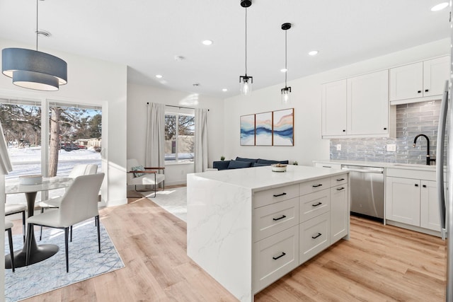 kitchen with sink, white cabinets, hanging light fixtures, stainless steel dishwasher, and light stone countertops