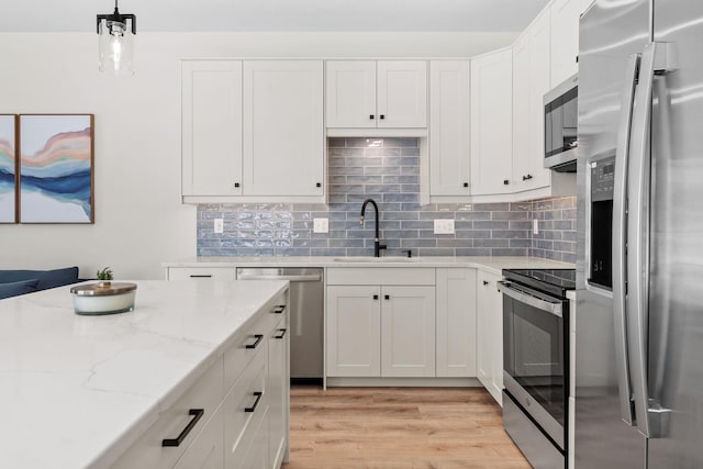 kitchen with stainless steel appliances, white cabinetry, hanging light fixtures, and sink