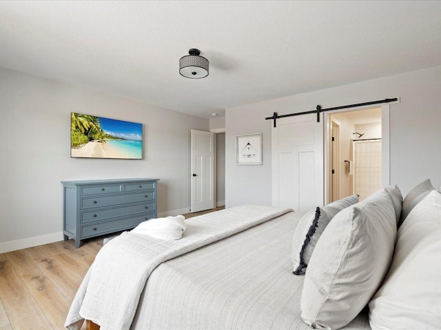 bedroom with ensuite bathroom, a barn door, and light hardwood / wood-style floors