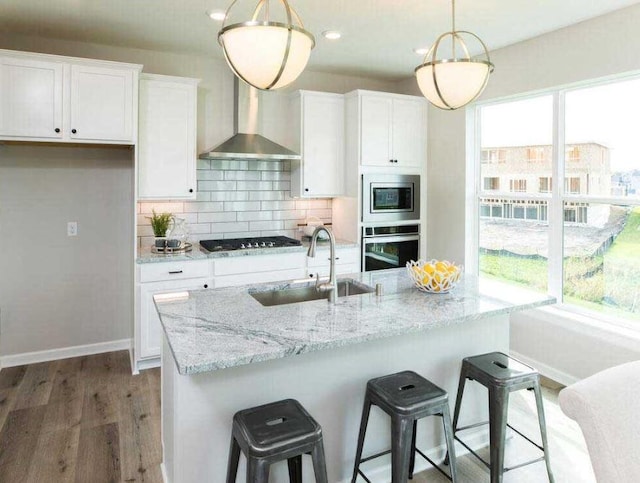 kitchen with white cabinetry, sink, hanging light fixtures, stainless steel appliances, and wall chimney range hood