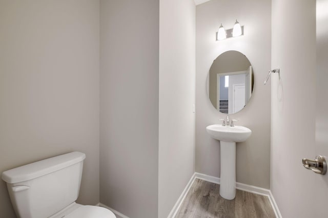 half bath featuring toilet, a sink, baseboards, and wood finished floors