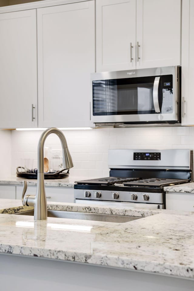 interior details featuring backsplash, appliances with stainless steel finishes, light stone countertops, and white cabinets