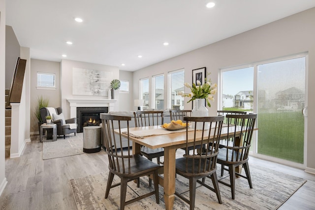 dining space featuring baseboards, recessed lighting, a glass covered fireplace, and light wood-style floors