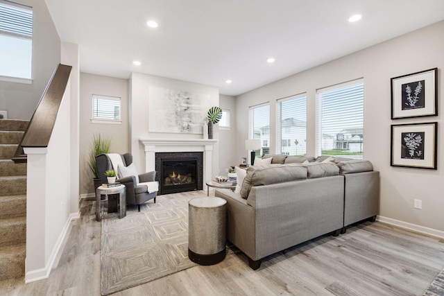 living room featuring recessed lighting, baseboards, stairway, light wood-type flooring, and a glass covered fireplace