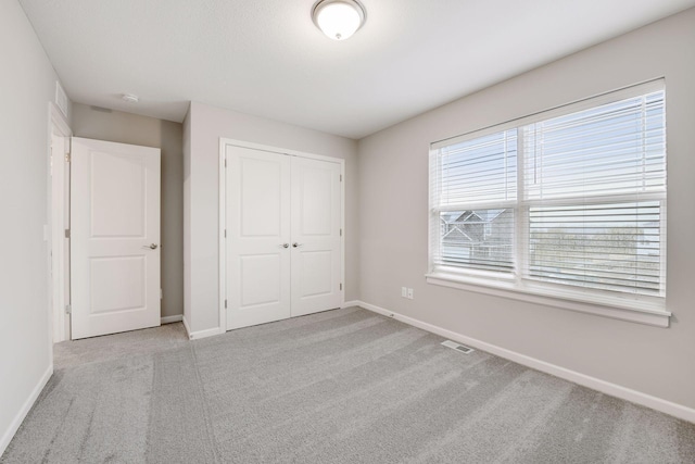 unfurnished bedroom with baseboards, a closet, visible vents, and light colored carpet