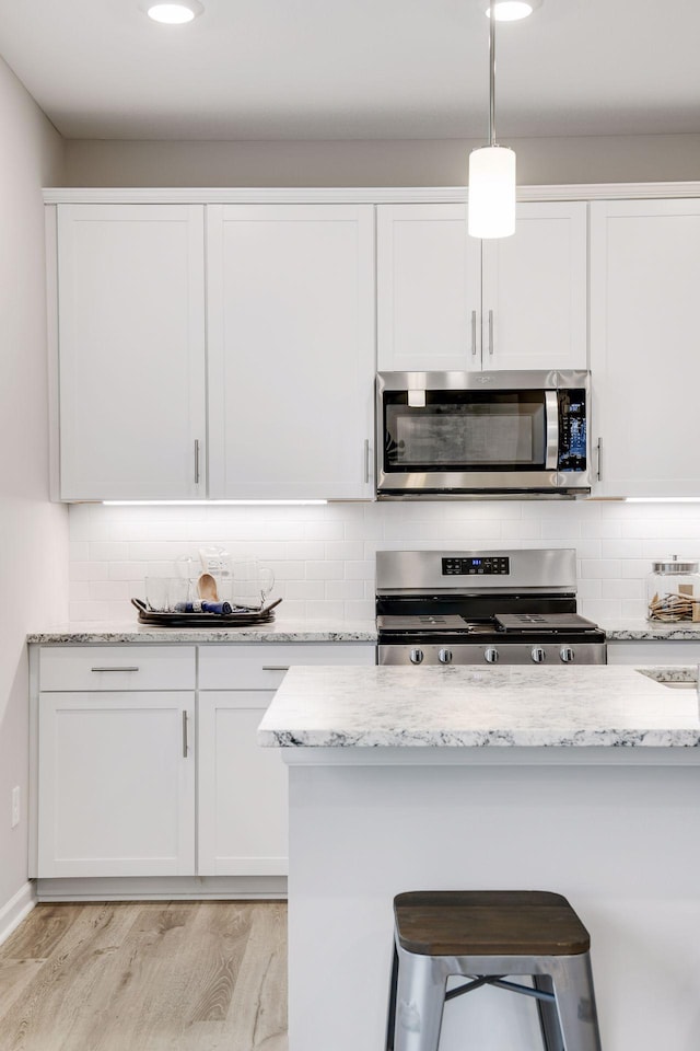 kitchen with light stone countertops, appliances with stainless steel finishes, white cabinets, and decorative light fixtures