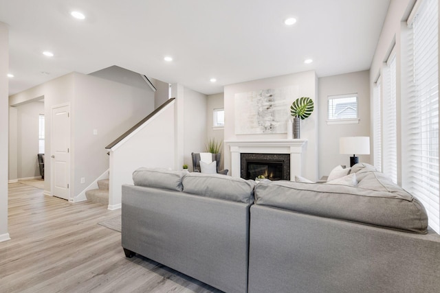 living area featuring light wood finished floors, recessed lighting, a glass covered fireplace, baseboards, and stairs