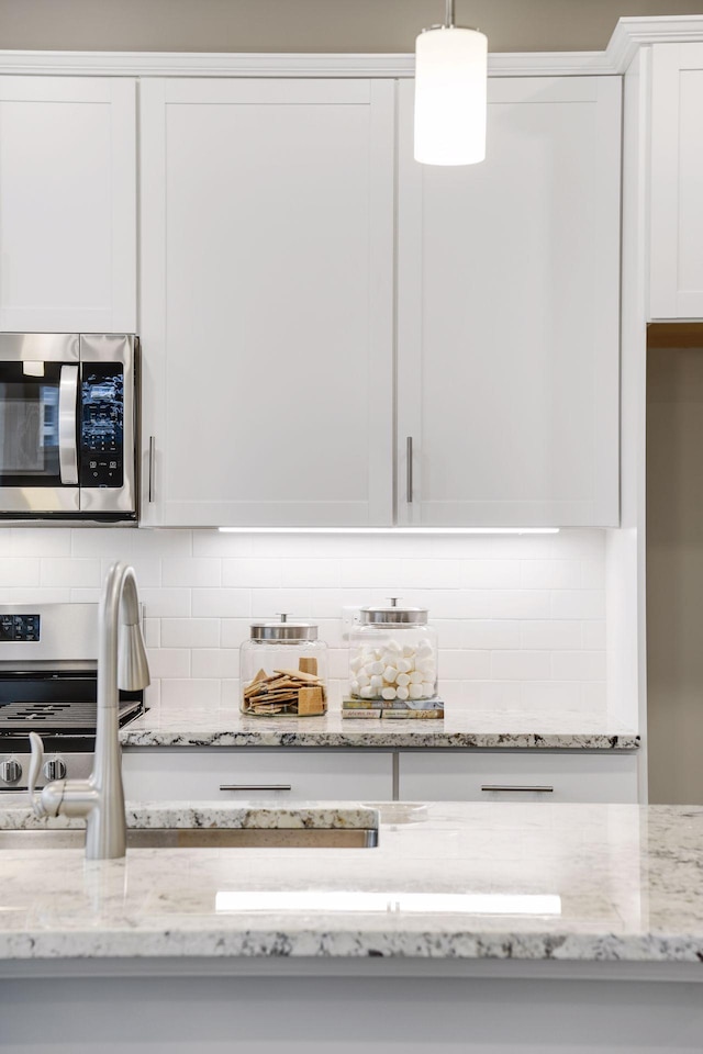 kitchen with light stone counters, white cabinets, tasteful backsplash, stainless steel microwave, and decorative light fixtures