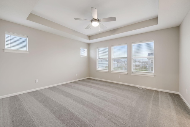 carpeted empty room featuring a tray ceiling, visible vents, ceiling fan, and baseboards