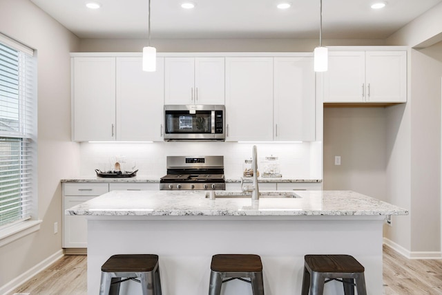 kitchen with tasteful backsplash, white cabinetry, stainless steel appliances, and light wood-style flooring