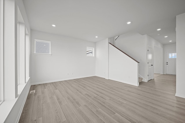 below grade area with baseboards, light wood-style flooring, stairs, a healthy amount of sunlight, and recessed lighting