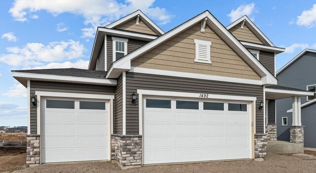 exterior space featuring an attached garage, stone siding, and roof with shingles