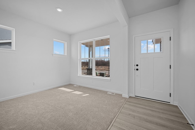 foyer featuring light colored carpet, visible vents, and baseboards