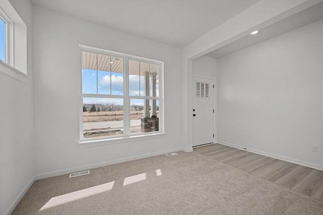 spare room with light colored carpet, visible vents, and baseboards