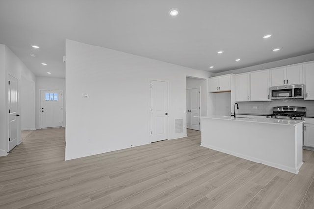 kitchen with a sink, stainless steel appliances, light wood-style floors, backsplash, and recessed lighting