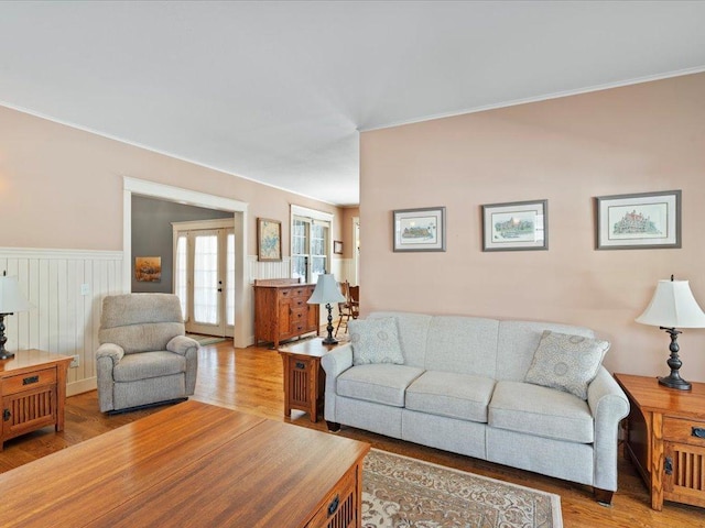 living area with a wainscoted wall, french doors, and light wood-style floors