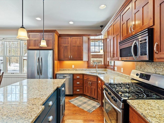 kitchen featuring light stone counters, light wood-style flooring, stainless steel appliances, a sink, and pendant lighting