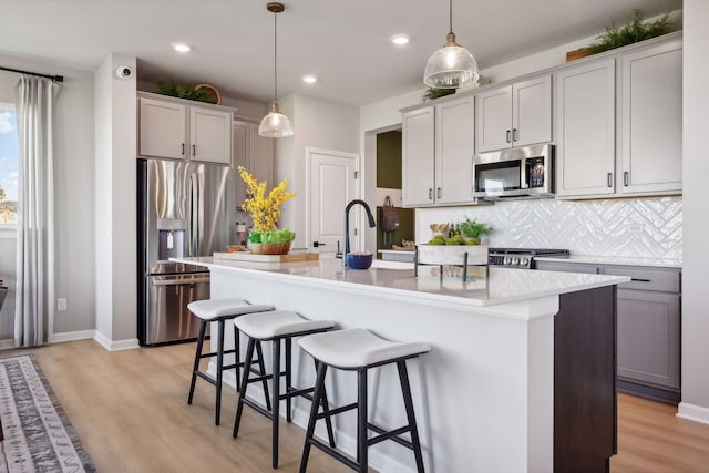 kitchen with stainless steel appliances, decorative light fixtures, gray cabinets, and an island with sink