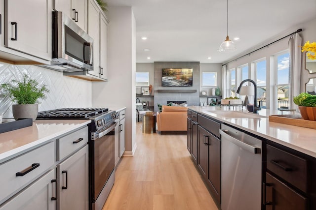 kitchen featuring sink, decorative light fixtures, stainless steel appliances, light hardwood / wood-style floors, and decorative backsplash