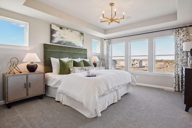 carpeted bedroom featuring multiple windows, a raised ceiling, and a chandelier