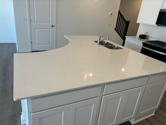 kitchen with dark wood-style floors, a large island, white cabinetry, a sink, and light stone countertops